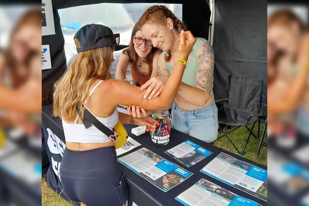 PETA Streetteam mit Stand auf dem Southside Festival kleben einer Interessierten ein Klebetattoo auf.